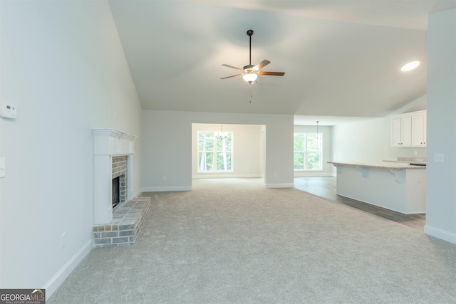 unfurnished living room with light carpet, high vaulted ceiling, a brick fireplace, and ceiling fan with notable chandelier