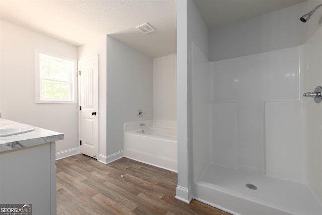 bathroom with vanity, hardwood / wood-style flooring, a textured ceiling, and plus walk in shower