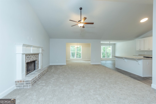 unfurnished living room featuring high vaulted ceiling, light hardwood / wood-style flooring, a brick fireplace, and ceiling fan with notable chandelier