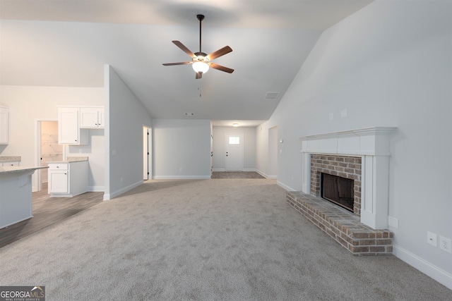 unfurnished living room featuring light carpet, a brick fireplace, high vaulted ceiling, and ceiling fan