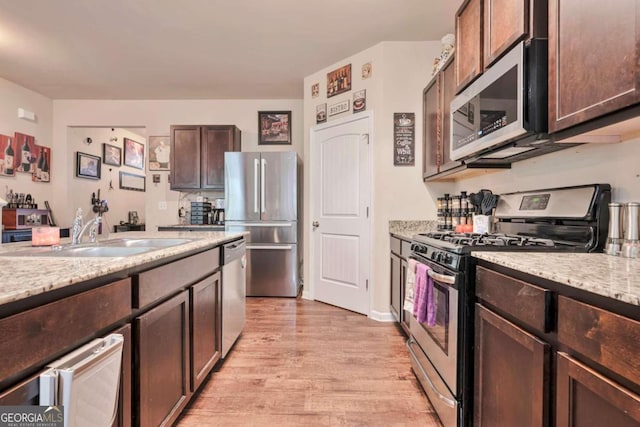 kitchen with sink, dark brown cabinetry, light wood-type flooring, appliances with stainless steel finishes, and light stone counters