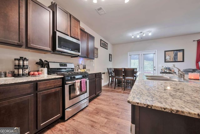 kitchen featuring appliances with stainless steel finishes, sink, light wood-type flooring, dark brown cabinetry, and light stone counters