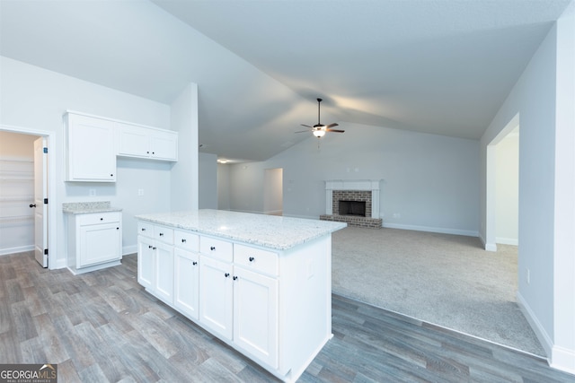 kitchen featuring vaulted ceiling, a brick fireplace, a center island, white cabinetry, and ceiling fan