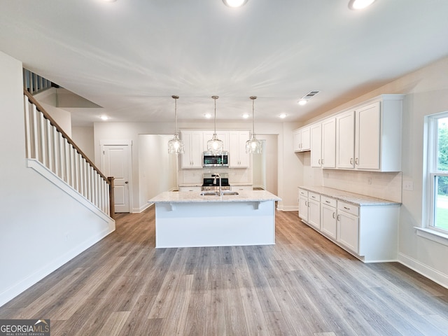 kitchen with an island with sink, white cabinets, hanging light fixtures, and light wood-type flooring