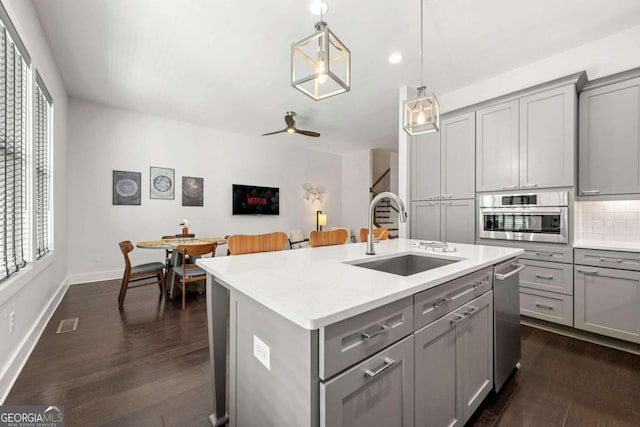 kitchen featuring gray cabinets, decorative light fixtures, a kitchen island with sink, and sink