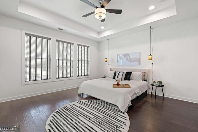 bedroom with ceiling fan, a tray ceiling, and dark hardwood / wood-style flooring