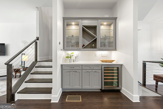 bar with wine cooler, dark wood-type flooring, gray cabinetry, and tasteful backsplash