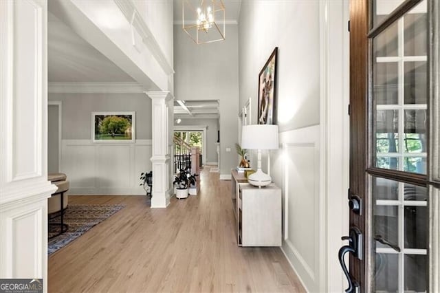 entryway with ornate columns, a notable chandelier, ornamental molding, and light hardwood / wood-style flooring