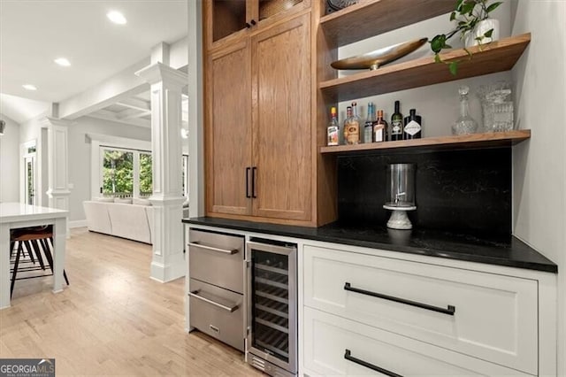 bar with beam ceiling, decorative columns, white cabinets, wine cooler, and light hardwood / wood-style flooring