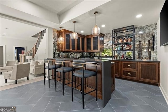 bar with dark brown cabinets, decorative light fixtures, dark tile patterned floors, and backsplash