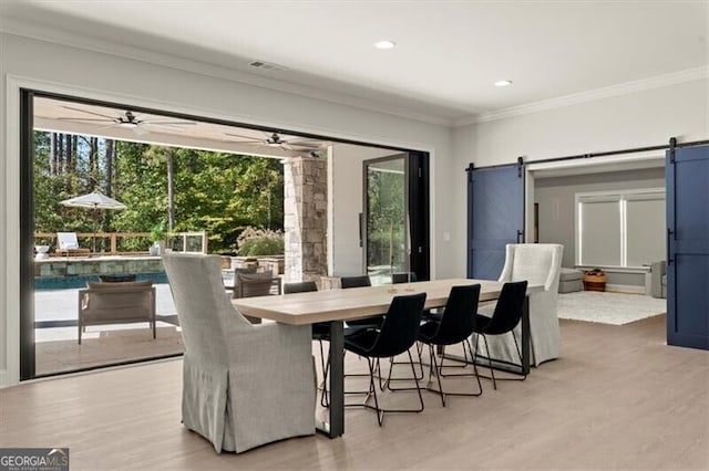 dining space with ceiling fan, crown molding, light wood-type flooring, and a barn door