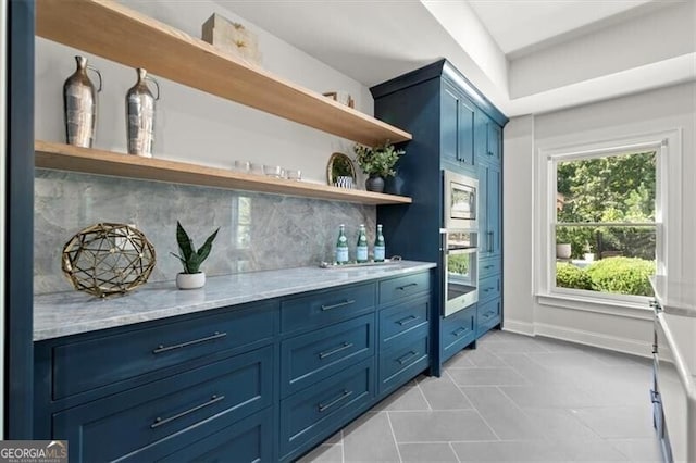 bar with light stone countertops, stainless steel microwave, light tile patterned flooring, backsplash, and blue cabinets