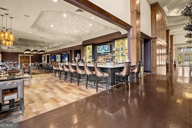 bar featuring pendant lighting, hardwood / wood-style flooring, a towering ceiling, and a raised ceiling