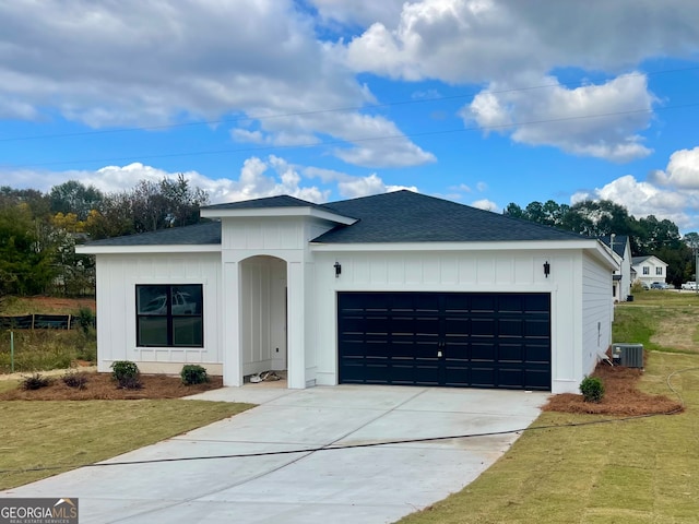 view of front of home featuring a front yard, central AC, and a garage