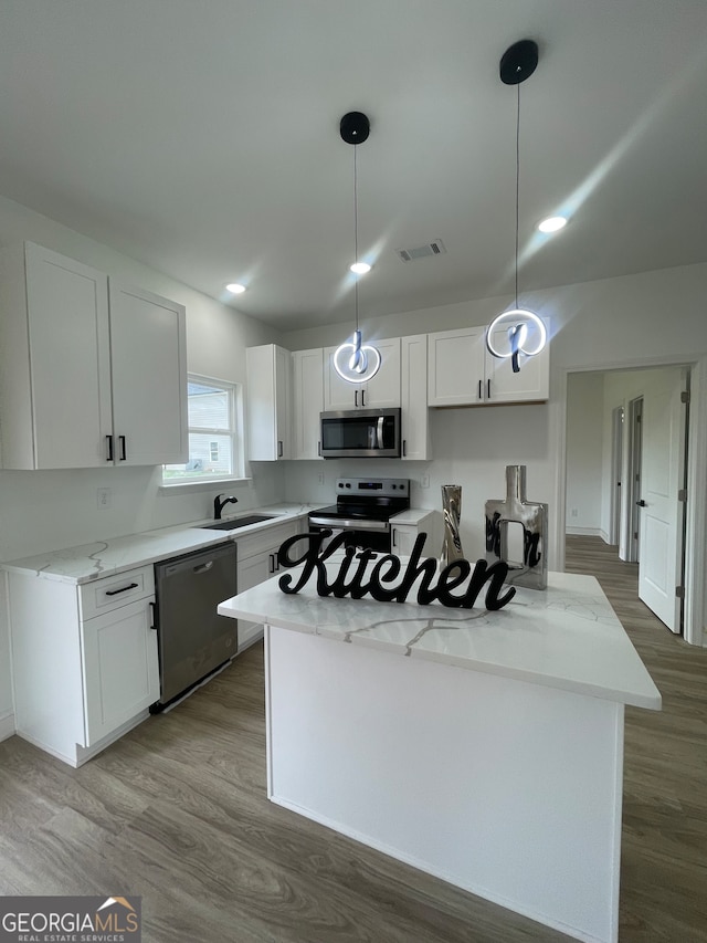 kitchen with appliances with stainless steel finishes, light stone counters, wood-type flooring, decorative light fixtures, and white cabinetry