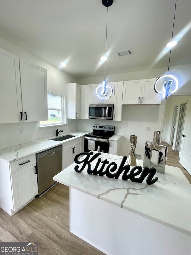 kitchen featuring light stone counters, stainless steel appliances, decorative light fixtures, light hardwood / wood-style floors, and white cabinetry