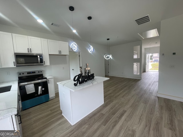 kitchen with light stone countertops, appliances with stainless steel finishes, wood-type flooring, white cabinets, and a kitchen island