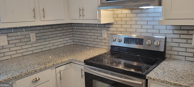 kitchen with light stone countertops, stainless steel electric range, exhaust hood, and white cabinets