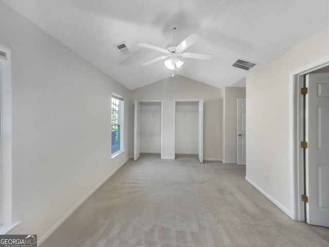 unfurnished bedroom with multiple closets, light colored carpet, vaulted ceiling, and ceiling fan