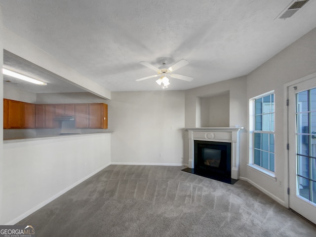 unfurnished living room with ceiling fan, carpet flooring, a textured ceiling, and beam ceiling