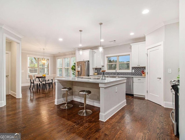 kitchen with a center island with sink, white cabinets, decorative light fixtures, appliances with stainless steel finishes, and dark hardwood / wood-style flooring