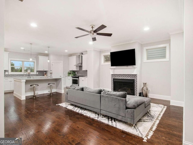 living room featuring ornamental molding, dark wood-type flooring, a tiled fireplace, and ceiling fan