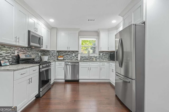 kitchen with appliances with stainless steel finishes, backsplash, white cabinetry, light stone counters, and dark hardwood / wood-style floors