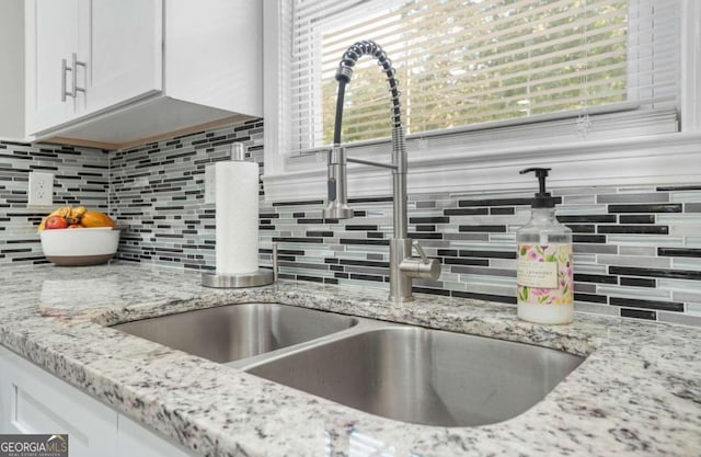 kitchen with white cabinets, tasteful backsplash, sink, and light stone counters