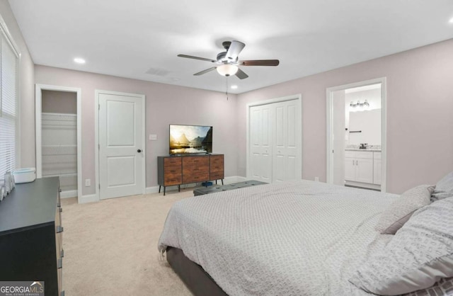 carpeted bedroom featuring two closets, connected bathroom, and ceiling fan