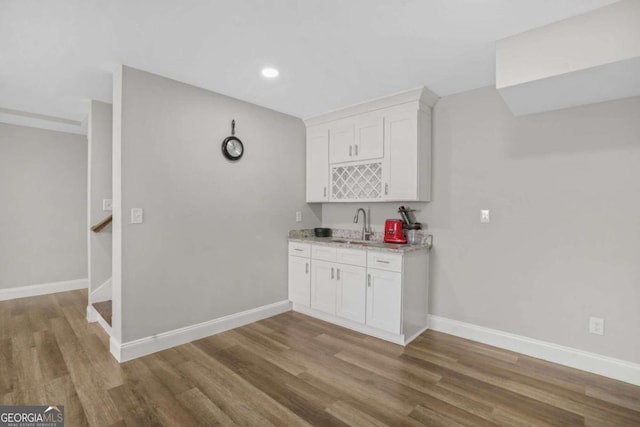 kitchen with white cabinetry, hardwood / wood-style flooring, light stone countertops, and sink