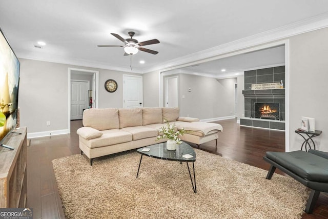 living room with dark wood-type flooring, a tiled fireplace, crown molding, and ceiling fan