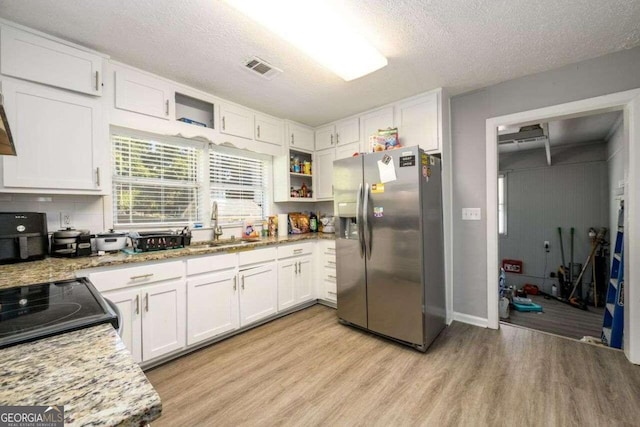 kitchen featuring light stone countertops, a textured ceiling, stainless steel fridge, white cabinets, and light hardwood / wood-style flooring