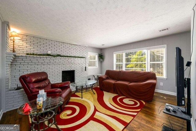 living room featuring a textured ceiling, brick wall, a fireplace, and dark hardwood / wood-style flooring