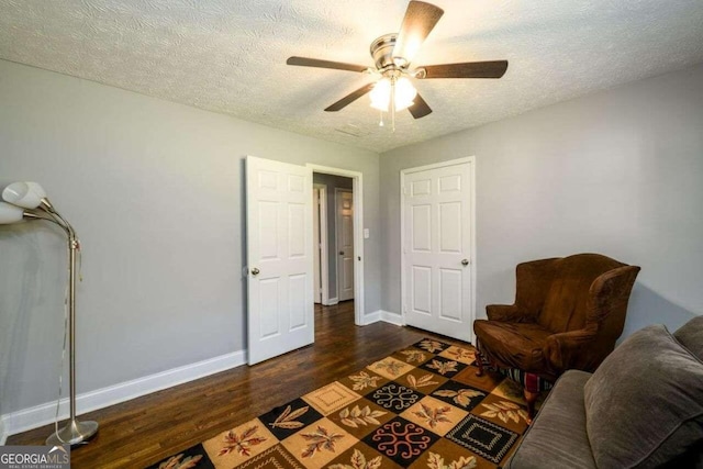 living area with ceiling fan, a textured ceiling, and dark hardwood / wood-style floors