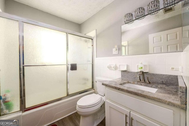 full bathroom with toilet, wood-type flooring, vanity, tile walls, and combined bath / shower with glass door