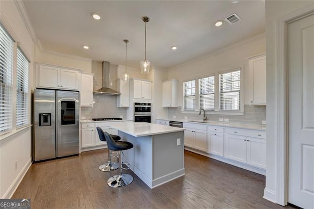 kitchen with white cabinets, hanging light fixtures, wall chimney exhaust hood, a kitchen island, and stainless steel appliances