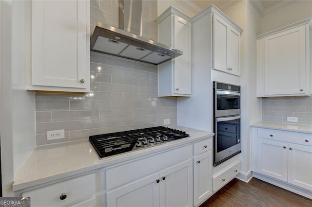 kitchen featuring white cabinetry, light stone countertops, wall chimney exhaust hood, stainless steel appliances, and tasteful backsplash