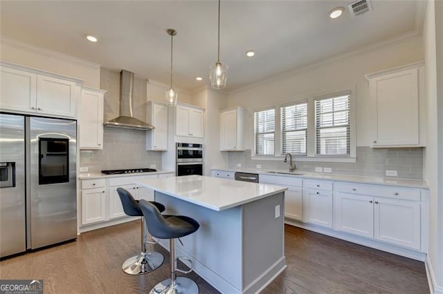 kitchen with white cabinetry, sink, wall chimney range hood, a kitchen island, and appliances with stainless steel finishes