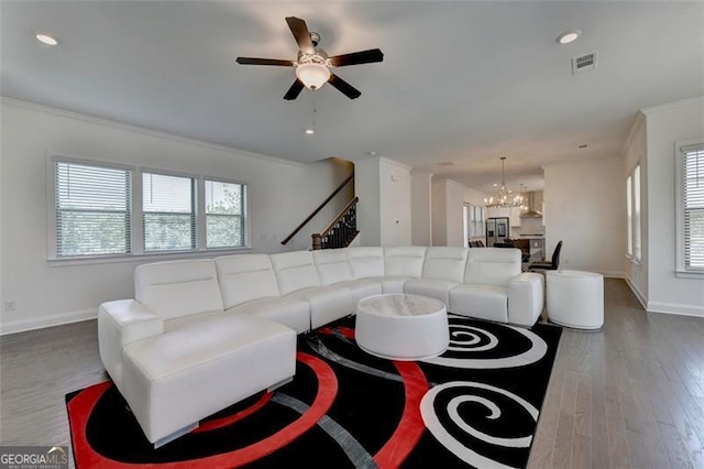 living room with wood-type flooring, ceiling fan with notable chandelier, and ornamental molding