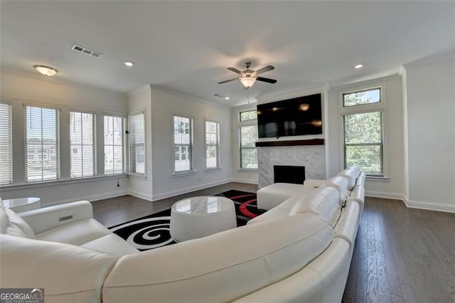 living room with ceiling fan, a large fireplace, ornamental molding, and dark wood-type flooring