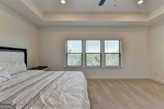 bedroom with a raised ceiling, light carpet, and ceiling fan