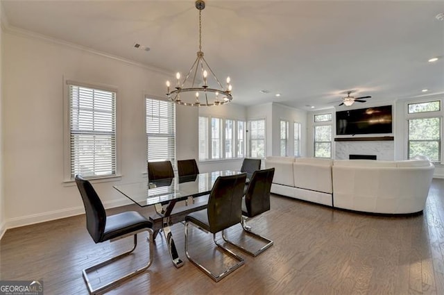 dining room with hardwood / wood-style flooring, ceiling fan with notable chandelier, ornamental molding, and a fireplace