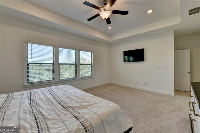 carpeted bedroom with ceiling fan and a tray ceiling