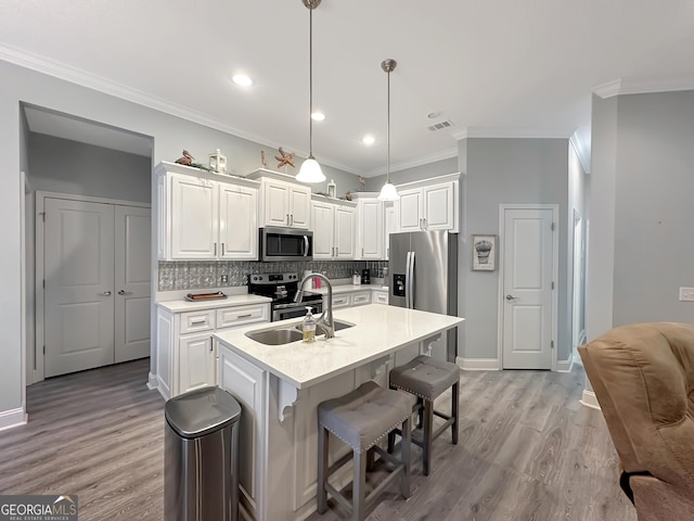 kitchen with appliances with stainless steel finishes, sink, white cabinets, hanging light fixtures, and a center island with sink