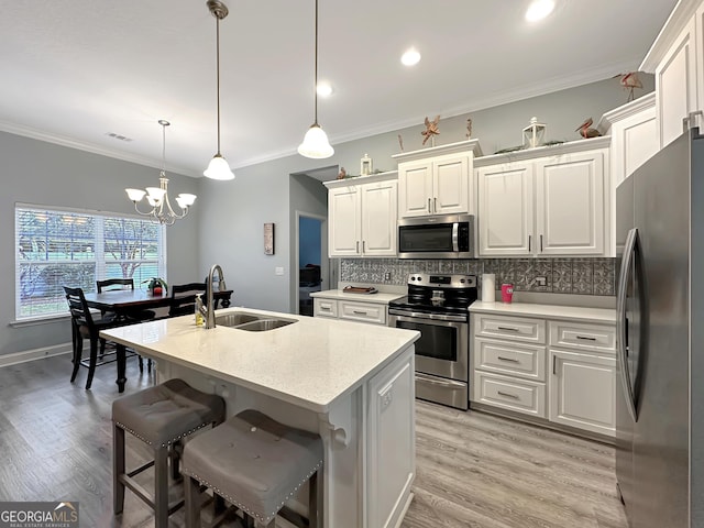 kitchen with appliances with stainless steel finishes, decorative light fixtures, sink, white cabinets, and a kitchen island with sink