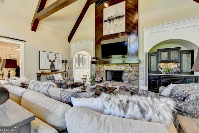 living room with beam ceiling, a stone fireplace, and high vaulted ceiling