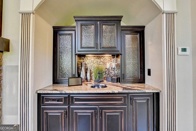 bar with light stone counters, tasteful backsplash, sink, and ornate columns