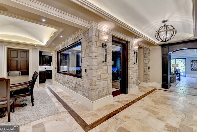 corridor featuring decorative columns, ornamental molding, a tray ceiling, and an inviting chandelier