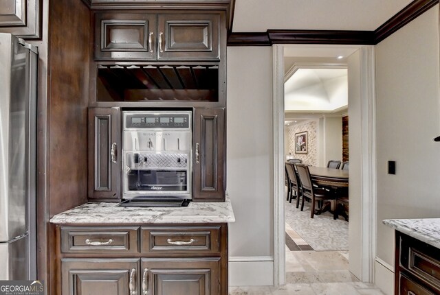 kitchen featuring light stone counters, dark brown cabinetry, ornamental molding, and stainless steel refrigerator