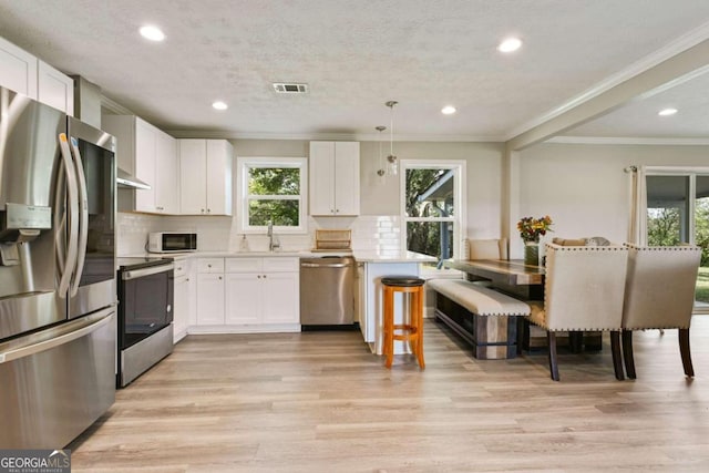 kitchen with light hardwood / wood-style floors, white cabinetry, stainless steel appliances, and pendant lighting